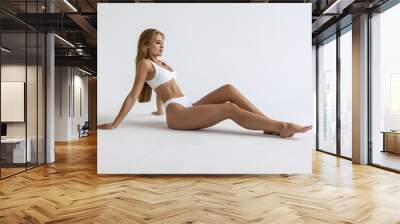 Perfect young woman with sporty body in underwear sitting on floor posing on white studio background. Body care, spa, female beauty concept Wall mural